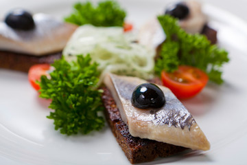 Sliced black bread and herring on a white plate