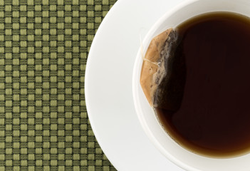 Top close view of a cup of decaffeinated black tea with a tea bag atop a green cloth place mat.