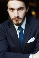 Head and shoulders portrait of handsome bearded man wearing elegant business suit, looking confidently at camera with neutral face expression