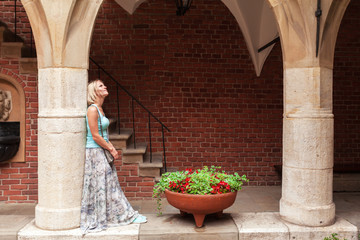 Beautiful young woman stands leaning on a column in an arched passage of the ancient university building in Krakow. Poland. Studying abroad. Student life. The ancient universities of Europe