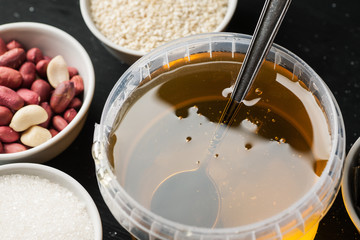 Honey jar and ceramic bowls with sesame, peanuts and sugar on a black wooden table
