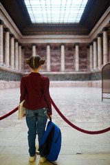 Girl with school-bag looking at ancient colonnade in museum