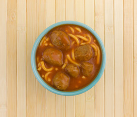 Bowl of spaghetti and meatballs on a wood place mat.