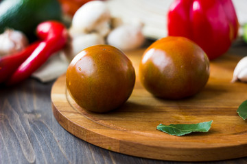 Kumato tomatoes on wooden board surrounded by vegetables.