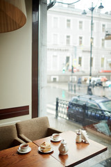 Two cups of tea, sugar-bowl, brewing-teapot and sandwiches on wooden table in empty cafe