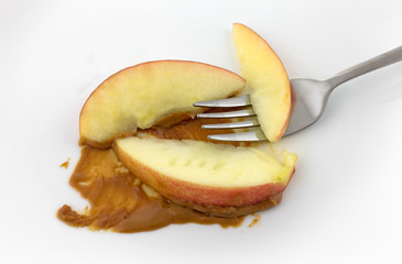 Apple slices with peanut butter and a fork on a white plate.