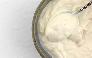 Top close view of apple Greek yogurt in a stoneware bowl with a spoon atop a white tablecloth.