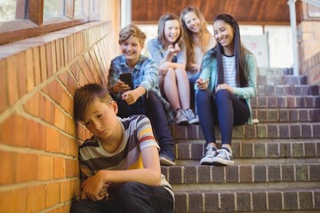 School friends bullying a sad boy in school corridor - obrazy, fototapety, plakaty