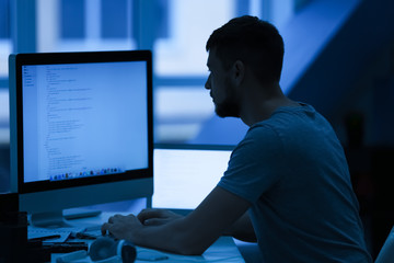 Handsome young programmer working at home late in evening