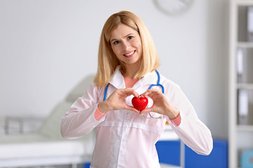 Female doctor with stethoscope holding heart, on blurred background