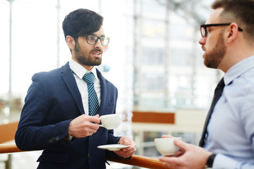 Serious businessmen having talk by cup of coffee at break