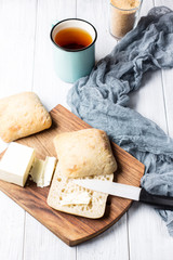 A cup of tea and ciabatta with butter on a white wooden background, soft selective focus, vertical, top view
