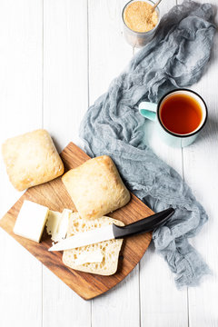 A cup of tea and ciabatta with butter on a white wooden background, soft selective focus, vertical, top view
