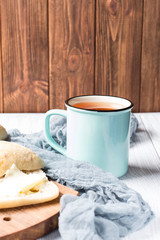 A cup of tea and ciabatta with butter on a white wooden background, soft selective focus, vertical 
