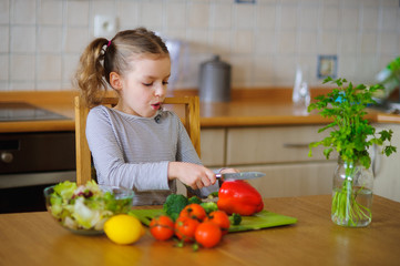 Cute girl of younger school age cuts vegetables and greens for salad.