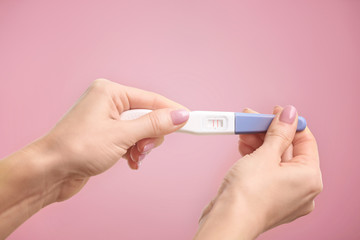 Pregnancy test in hands on color background