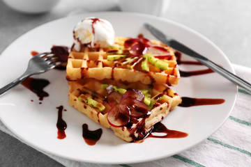 Delicious waffles with fruits, ice-cream and syrup on white plate