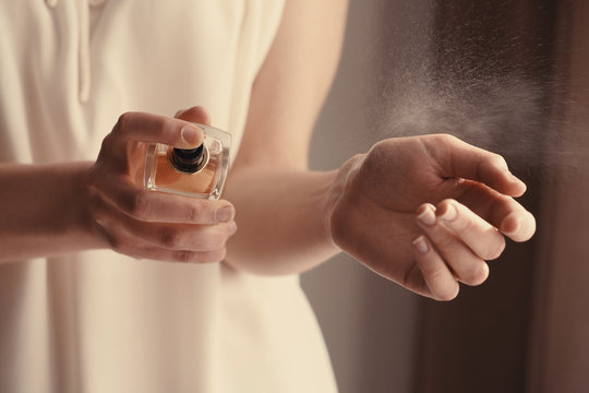 Beautiful young woman with bottle of perfume at home, closeup