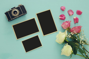 Top view of empty photo frames next to old camera and roses