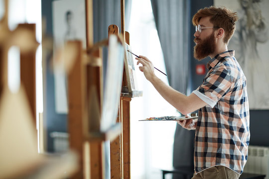 Young bearded student of art-school painting in workroom