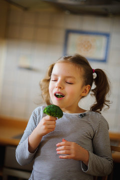Cute fair-haired girl eats fresh broccoli.