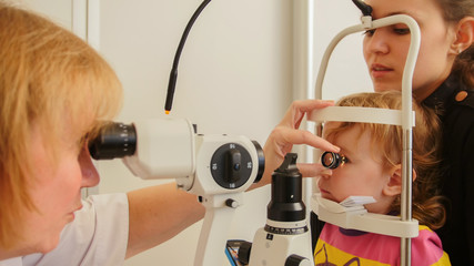 Child's healthcare - little girl with mommy in ophthalmological clinic checks eyesight