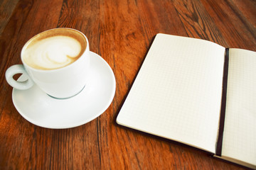 cup of coffee capuccino with note black book on the wood table like a hipster style