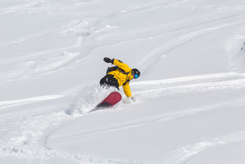 Male snowboarder snowboarding on fresh snow on ski slope on Sunny winter day in the ski resort in Georgia