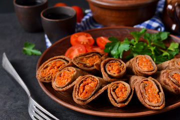 Pancakes made with liver stuffed with carrots and mushrooms on a black background