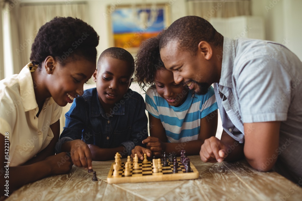 Wall mural family playing chess together at home in the living room