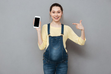 Happy pregnant woman pointing finger at blank screen mobile phone