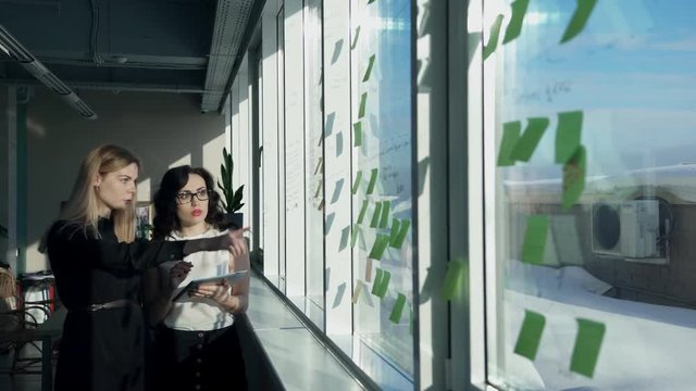 Two female office collate and recording in a computer window. At a special transparent coating made token entries. Employees blonde and brunette in glasses go and check the synopsis after the seminar