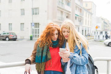 Two young women using smart phone outdoor  - technology, social network, communication concept