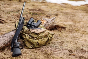 Tuinposter .Set van militaire jachtuitrusting met geweer in het bos tijdens het jachtseizoen. Bushcraft-, jacht- en wapenconcept © kaninstudio
