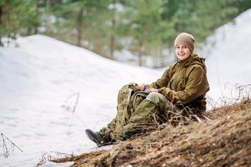 Hunter girl sitting with backpack and drinking water outdoor snow forest in background.