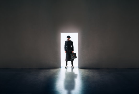 Man silhouette standing in the light of opening door in dark room