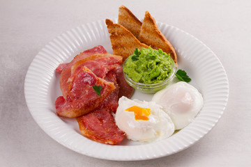 Bacon, poached eggs, mashed peas and toasts on white plate. Grilled rashers and eggs