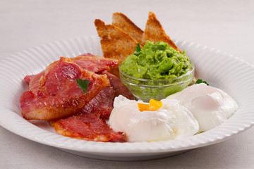 Bacon, poached eggs, mashed peas and toasts on white plate. Grilled rashers and eggs