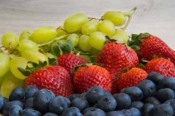Fresh fruits on a wooden background. Strawberries, grapes, blueberry closeup
