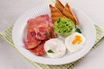 Bacon, poached eggs, mashed peas and toasts on white plate. Grilled rashers and eggs