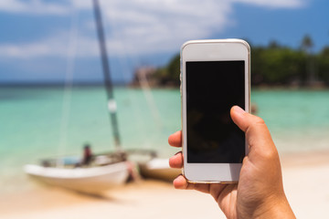 Summer vacation. Relax on the beach with the phone in hand. Man lying on the beach and enjoy your smartphone. The guy makes a photo of a yacht on a sea background.