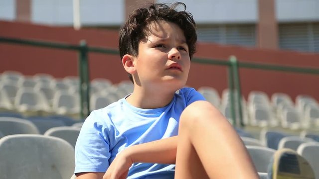 Young Boy  Sitting On Tribunes And Watching Football Game, Stadium