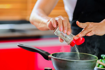Private Thai chef cooking in a modern style home kitchen. Making Thai food, adding paper, face hidden. Close up hands
