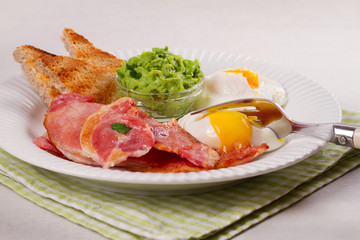 Bacon, poached eggs, mashed peas and toasts on white plate. Grilled rashers and eggs