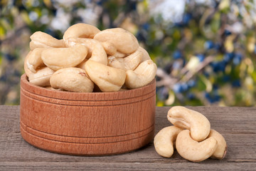 cashew nuts in a wooden bowl on the board with  blurred garden background