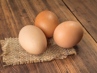Brown chicken eggs lay on a piece of burlap on a wooden table from the old boards. Three fresh chicken eggs close-up, background for advertising or Easter greetings, rustic style