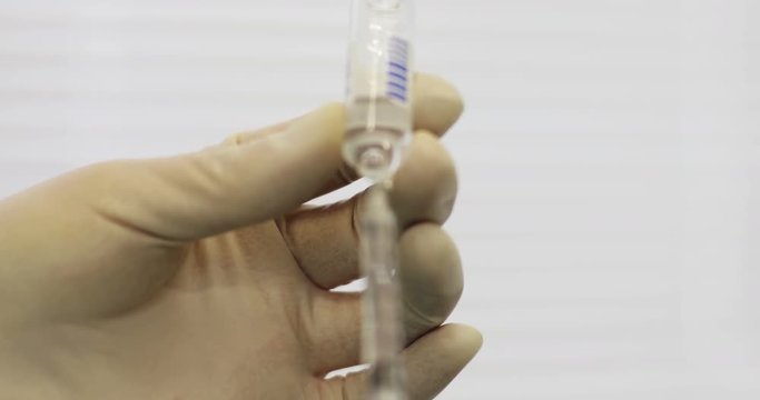 4K Close up of doctor's hands in gloves filling syringe with injection liquid.