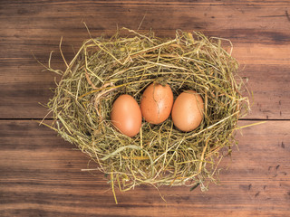 Brown eggs in hay nest. Rural eco background with brown chicken eggs and straw on the background of old wooden planks. Top view. Creative background for Easter cards, restaurant menu or design