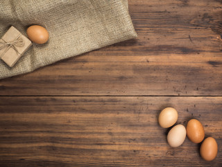 Brown chicken eggs and gift box lay on a piece of burlap on a wooden table from the old boards. Top view. Fresh chicken eggs close-up, background for advertising or Easter greetings, rustic style