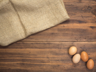 Brown chicken eggs lay on a piece of burlap on a wooden table from the old boards. Top view. Three fresh chicken eggs close-up, background for advertising or Easter greetings, rustic style